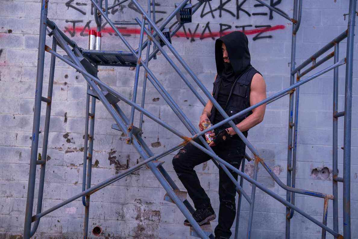 Freddy Miyares dans une hotte debout sur un échafaudage à côté d'un mur de graffitis dans une photo de DMZ