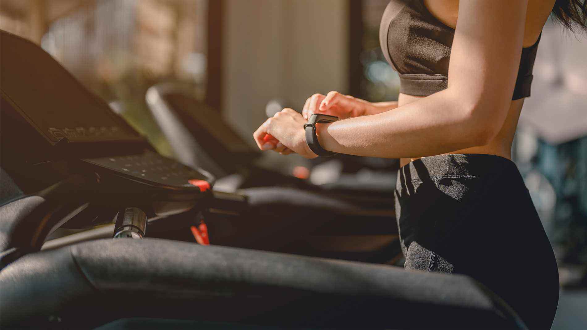 Image d'une femme regardant un tracker de fitness au poignet sur un tapis roulant