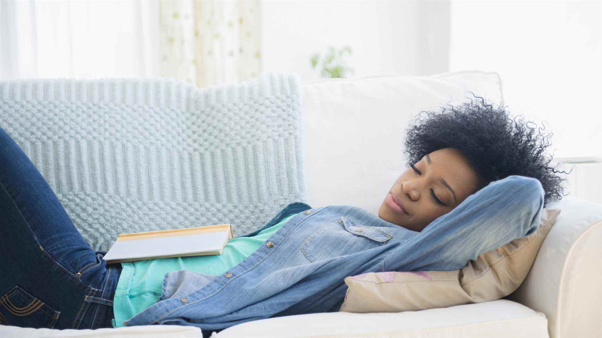 Une femme portant une chemise en jean fait la sieste sur son canapé