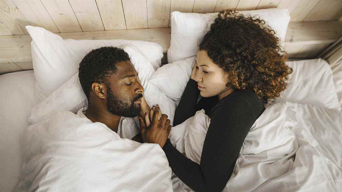 La femme regarde son associé dormant dans le lit