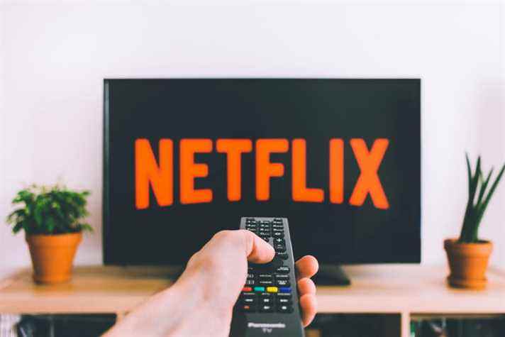 Une main pointe une télécommande vers un téléviseur affichant un écran de logo Netflix. 