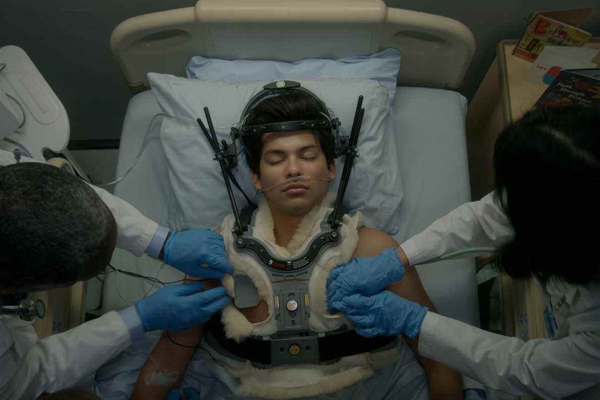 Un personnage de Cobra Kai allongé dans son lit avec une minerve pendant que les médecins travaillent sur lui