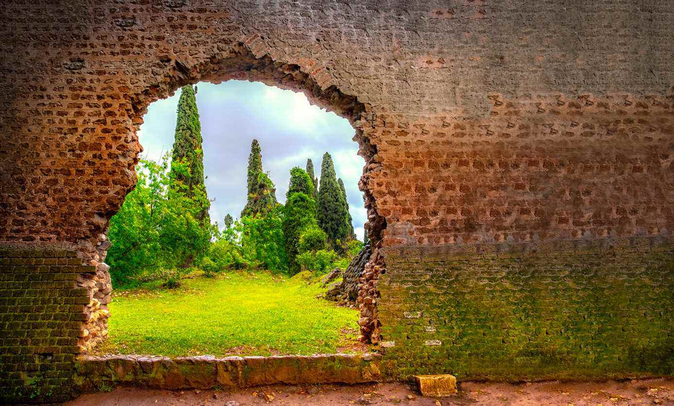 Photo d'un jardin verdoyant entrevu à travers un trou déchiqueté dans un mur de briques prise à Latina, Italie