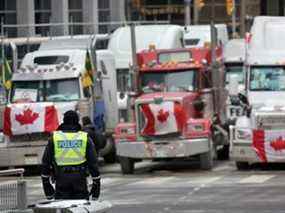 Un policier monte la garde près de camions participant à un blocus des rues du centre-ville près de l'édifice du Parlement alors qu'une manifestation menée par des camionneurs protestant contre les mandats de vaccination se poursuit le 16 février 2022 à Ottawa.