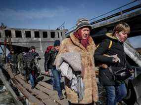 Des personnes traversent la rivière Irpin près d'un pont détruit alors qu'elles évacuent Irpin, au milieu de l'invasion russe de l'Ukraine, à l'extérieur de Kiev, le 12 mars 2022.