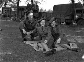 Trois membres des Forces armées canadiennes photographiés aux Pays-Bas juste après la fin de la Seconde Guerre mondiale.  Les deux sur la droite n'étaient pas autorisés à faire la guerre à moins qu'ils ne portent des nylons et des talons.