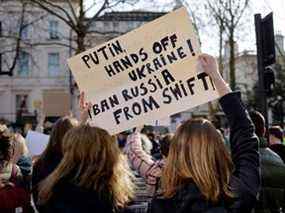 Des manifestants tiennent une pancarte appelant la Russie à être bannie du système bancaire Swift alors qu'ils assistent à un rassemblement de protestation devant l'ambassade de Russie à Londres, le 26 février 2022.