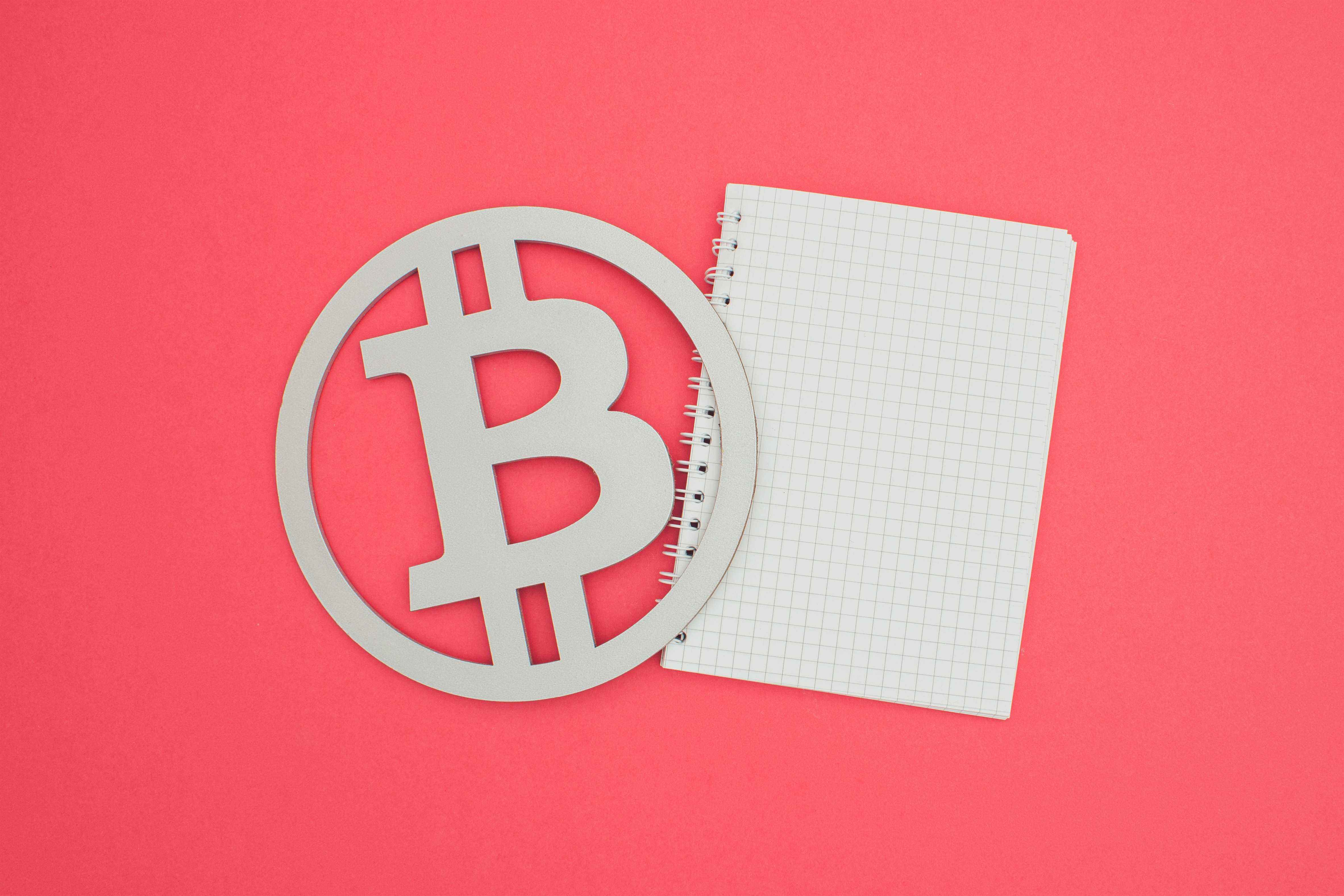 Image d'un symbole Bitcoin et d'un carnet blanc sur fond saumon.