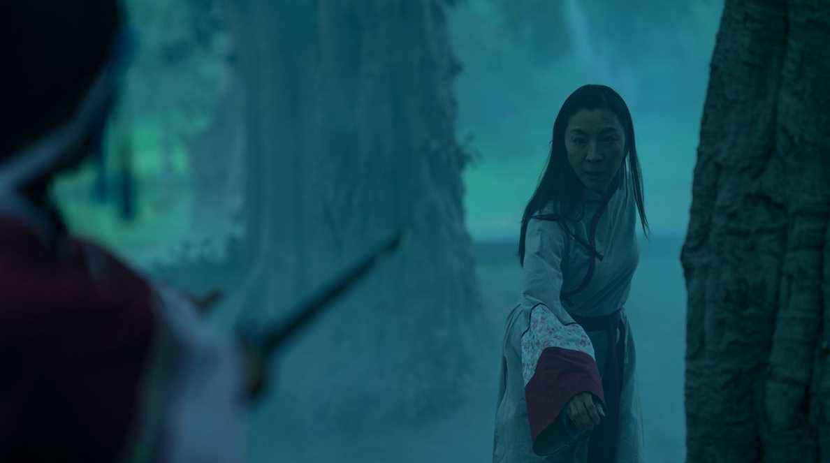 Michelle Yeoh, en tenue de hanfu d'époque, recule dans une forêt alors qu'un assaillant hors écran lui pointe une épée dans Everything Everywhere All At Once