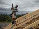 Un ouvrier cloue du contreplaqué sur le toit d'une maison en construction à Edmonton.