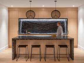Une cuisine secondaire avec du marbre noir ondulé, du chêne blanc et un éclairage doux est l'endroit où le désordre de la cuisine est caché lorsque les propriétaires se divertissent.