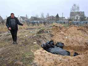 Un homme fait un geste vers une fosse commune dans la ville de Bucha, au nord-ouest de la capitale ukrainienne Kiev, le 3 avril 2022.