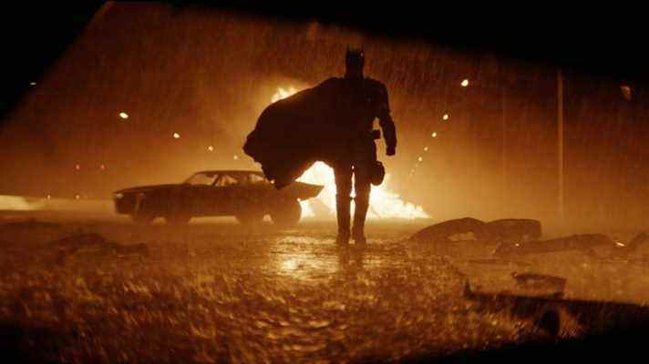 Batman s'approche de la caméra dans une rue pluvieuse avec un feu en arrière-plan.