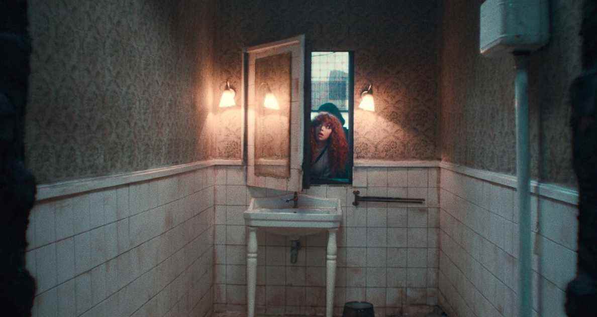 Nadia passe la tête à travers un mur en poussant un miroir comme une porte