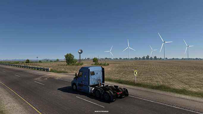 American Truck Simulator Texas - Une cabine de camion roule sur une route à deux voies avec des champs et des éoliennes en arrière-plan.
