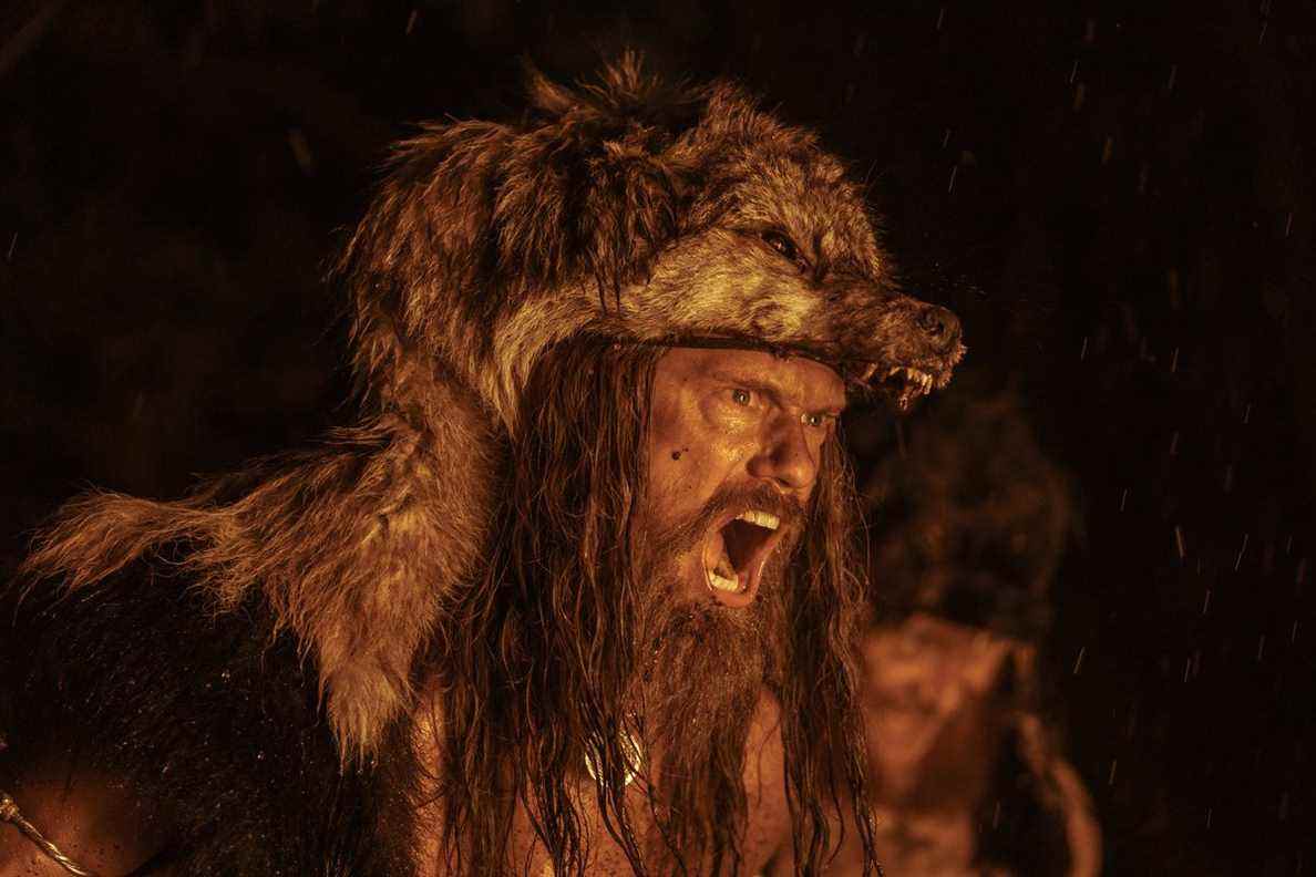 Alexander Skarsgard, vêtu d'une peau de loup, hurle lors d'un rituel de guerre à la lumière du feu dans The Northman