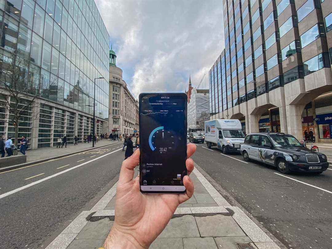 Main tenant un smartphone avec des bâtiments de rue et de verre en arrière-plan.