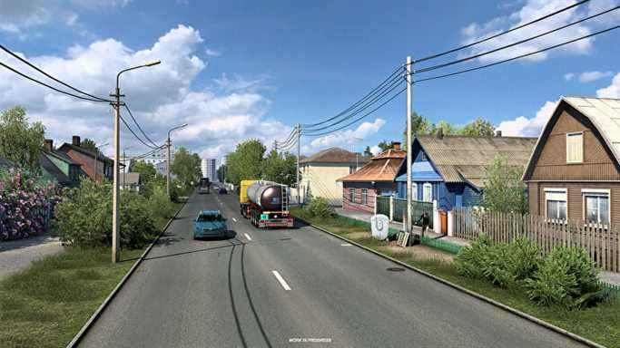 Euro Truck Sim 2 Russie - Des camions et des voitures roulent sur une route à deux voies entre des rangées de maisons colorées.