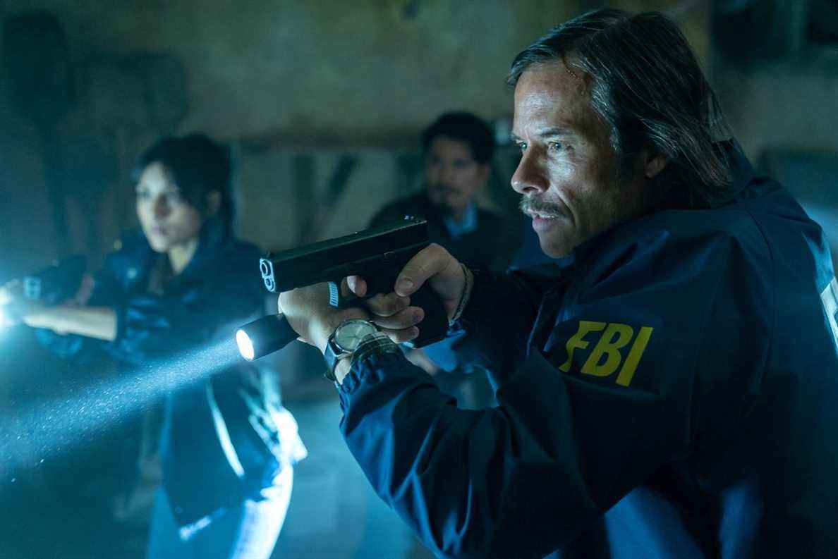 Guy Pearce dans une veste du FBI brandit un pistolet et une lampe de poche dans le film Memory.