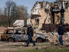 Des hommes marchent près d'une voiture incendiée et d'une maison endommagée dans le village de Bohdanivka, au nord-est de Kiev, le jeudi 14 avril 2022, au milieu de l'invasion russe lancée contre l'Ukraine.