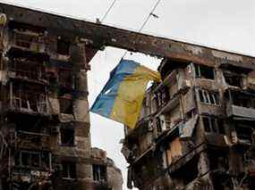 Une vue montre un drapeau ukrainien déchiré accroché à un fil devant un immeuble détruit lors du conflit Ukraine-Russie dans la ville portuaire méridionale de Marioupol, en Ukraine, le jeudi 14 avril 2022.