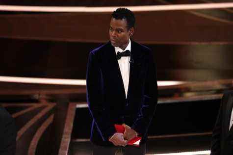 Chris Rock tient une enveloppe rouge alors qu'il se tient sur la scène des Oscars 2022