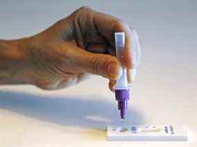 Une personne presse une goutte de solution de test dans un appareil de test rapide d'antigène COVID-19.