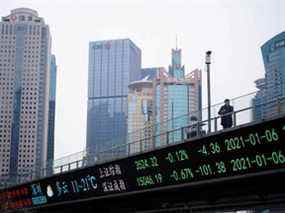 Un homme se tient sur un viaduc avec une carte électronique montrant les indices boursiers de Shanghai et de Shenzhen dans le quartier financier de Lujiazui à Shanghai, en Chine.