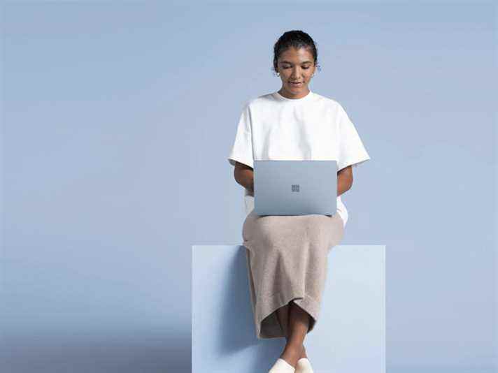 Une femme utilisant le Microsoft Surface Laptop 4 assise sur un bloc.