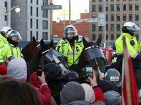 Des manifestants se tiennent devant des policiers canadiens à cheval, alors que des camionneurs et des partisans protestent contre les mandats de vaccination à Ottawa le 18 février 2022.