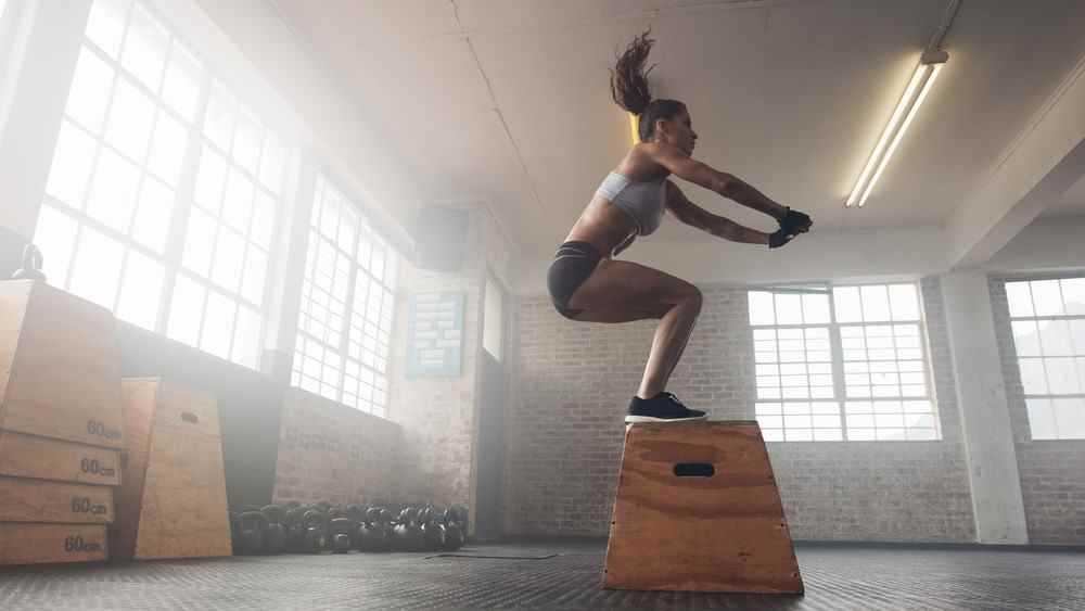 une photo d'une femme faisant un saut accroupi dans la salle de gym
