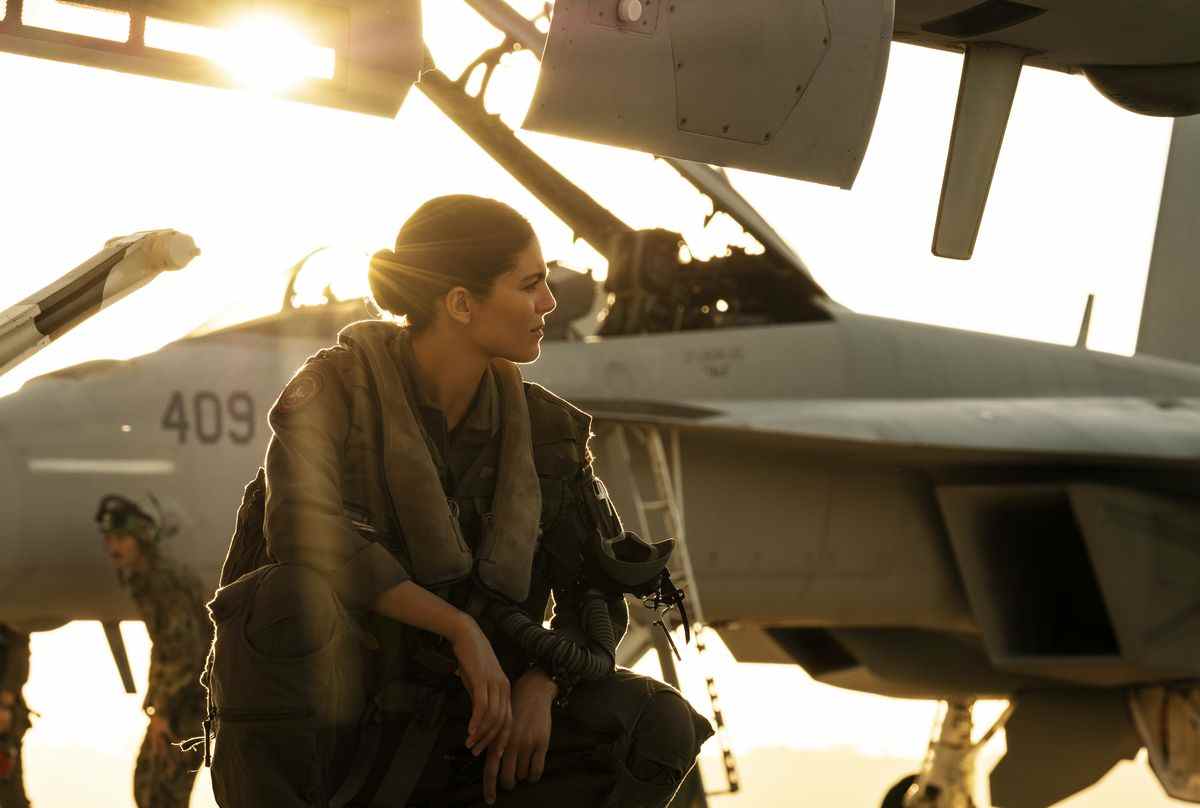 Phoenix (Monica Barbaro) s'accroupit près d'avions de chasse avec le soleil derrière elle