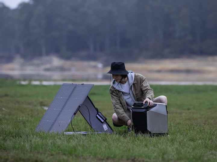 Un campeur utilise un EcoFlow Wave avec un panneau solaire à l'extérieur.