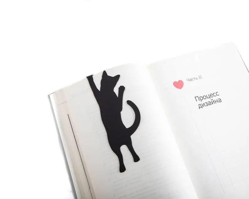 Image d'un signet en métal noir.  Il a la forme d'un chat tenant le haut d'une page de livre. 