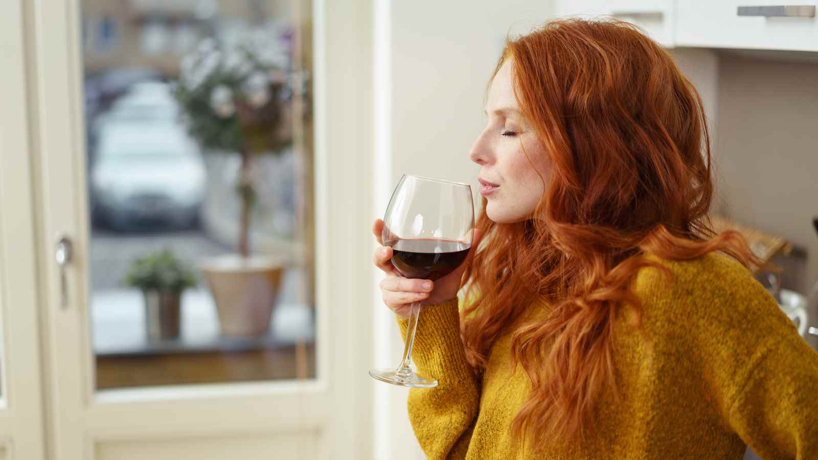 Une femme aux cheveux rouges boit un verre de vin rouge