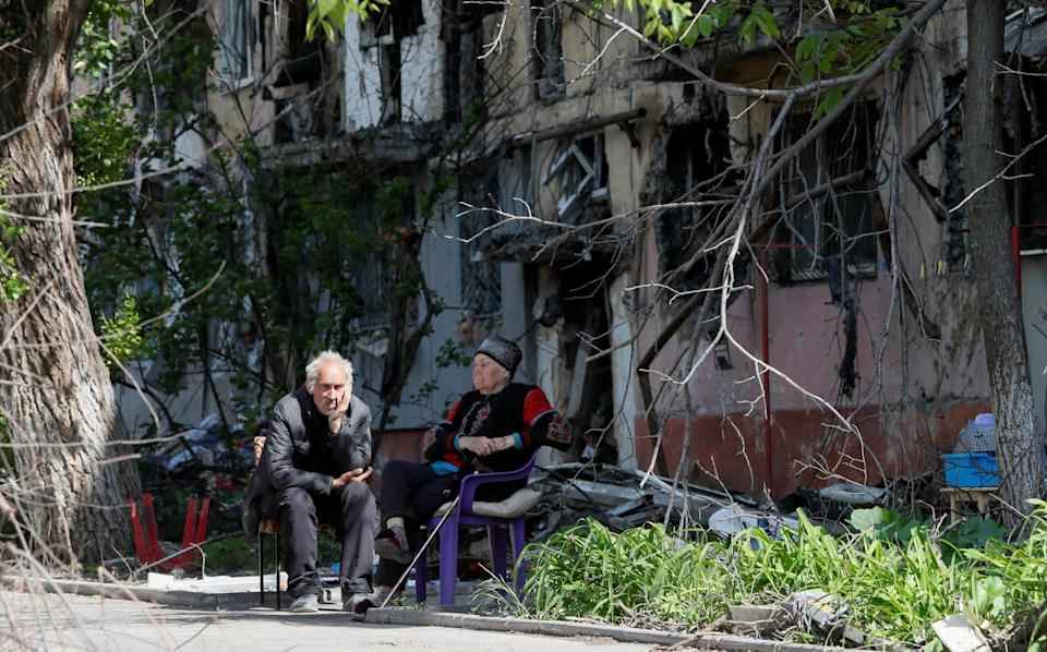 Les résidents locaux sont assis dans une cour près d'un immeuble fortement endommagé dans la ville portuaire méridionale de Marioupol, en Ukraine - REUTERS/Alexander Ermochenko