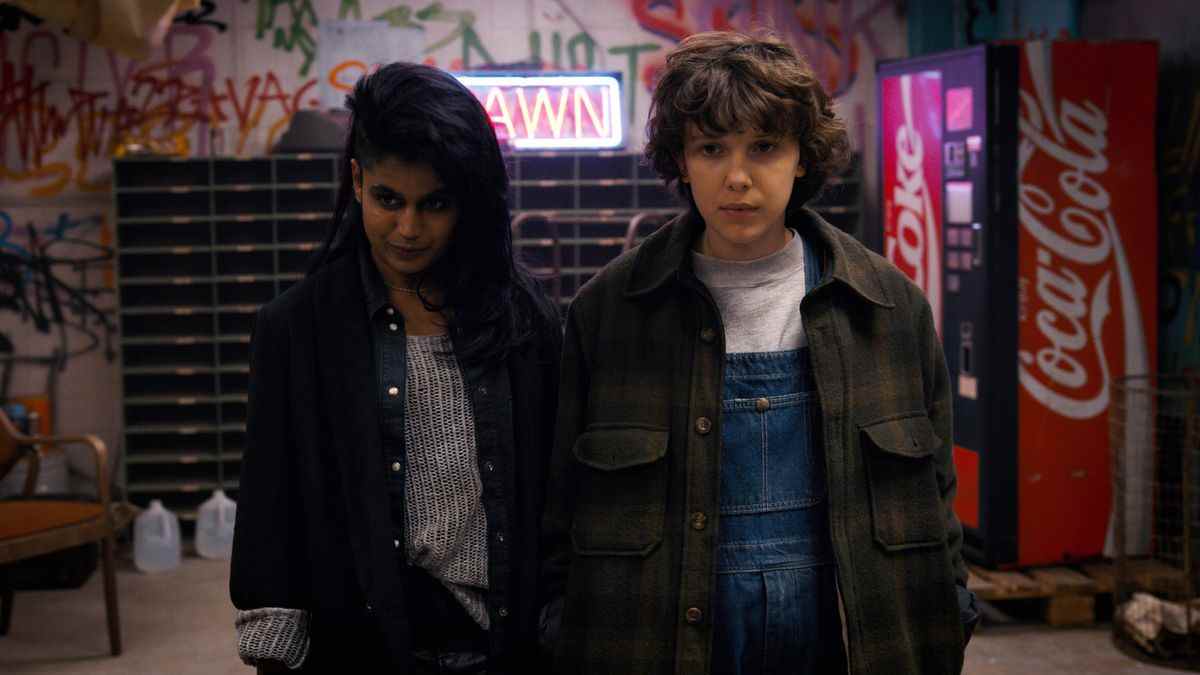 Kali (jouée par Linnea Berthelsen) et Eleven (jouée par Millie Bobby Brown) se tiennent côte à côte dans un loft couvert de graffitis.