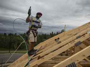 Un ouvrier cloue du contreplaqué sur le toit d'une maison en construction à Edmonton.