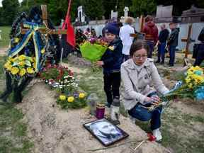 Les gens rendent hommage à côté des tombes du cimetière de Lychakiv où les personnes tuées lors de l'invasion russe de l'Ukraine sont enterrées lors de la célébration de la Journée des héros des cent célestes, à Lviv, en Ukraine, le 22 mai 2022.
