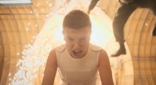 Medium-close shot of a child wearing a white vest and screaming while sparks fly and a figure is thrown backward behind her; still of Millie Bobby Brown in "Stranger Things 4."