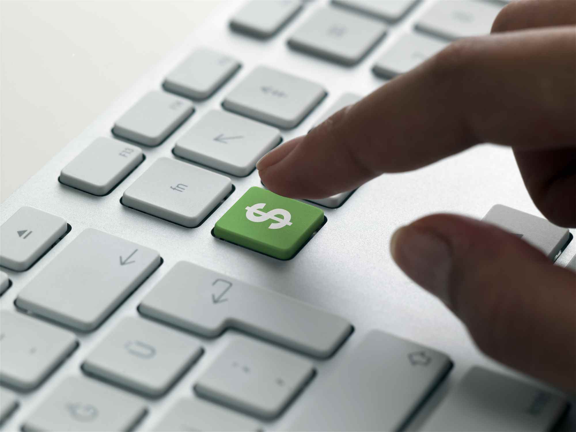 doigt sur le point d'appuyer sur la touche verte du signe dollar sur un clavier, ce qui signifie les dépenses informatiques en 2022