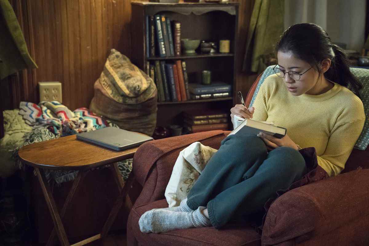 Leah Lewis dans le rôle d'Alice Wu assise dans un fauteuil et écrivant sur un livre à couverture rigide dans The Half of It.