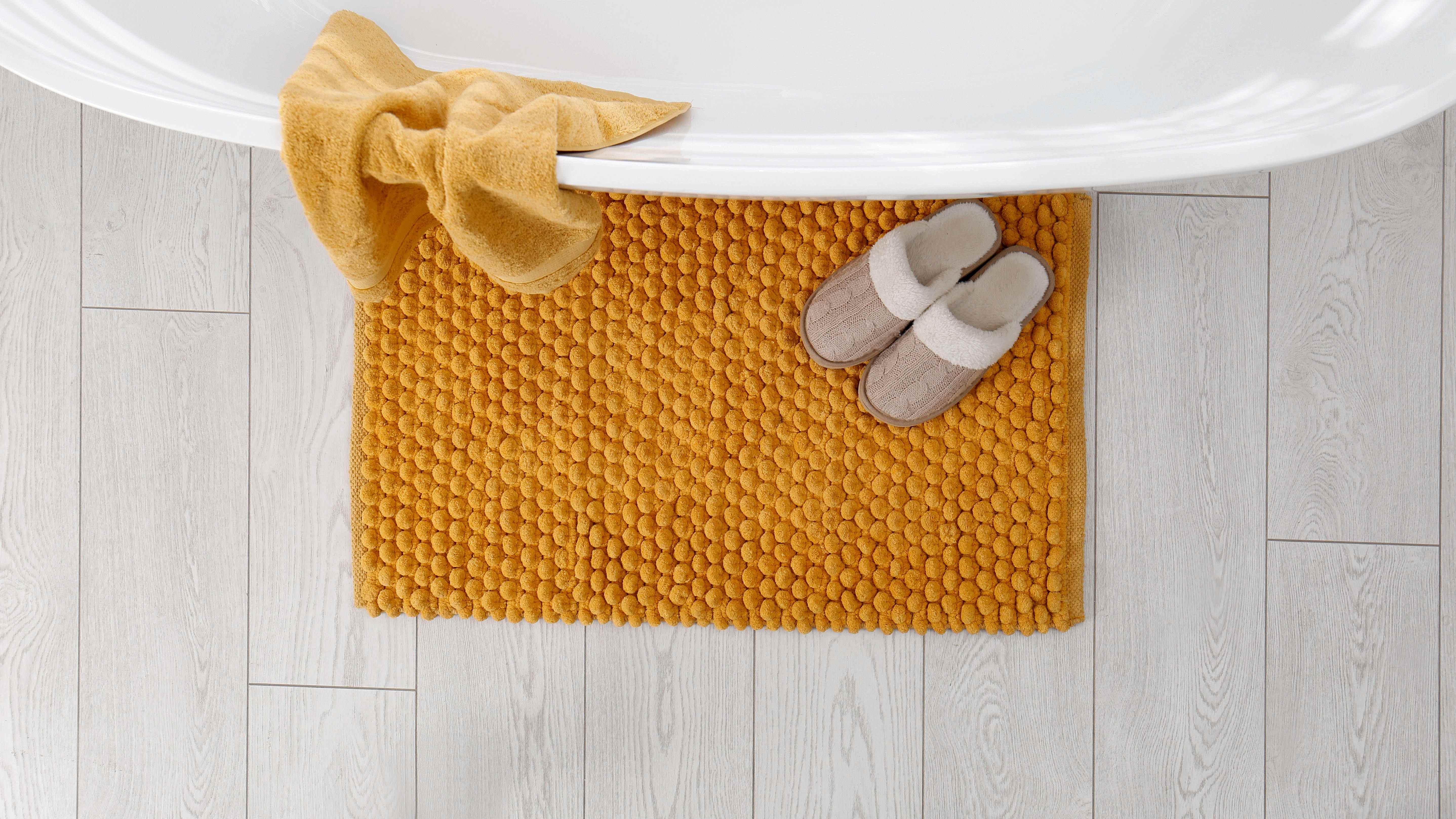 Un tapis de bain jaune à côté d'une baignoire avec une paire de chaussons et une serviette