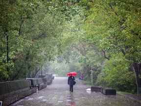 Un piéton se promène le long du sentier de la rivière à Eau Claire alors que de fortes pluies tombent lundi.