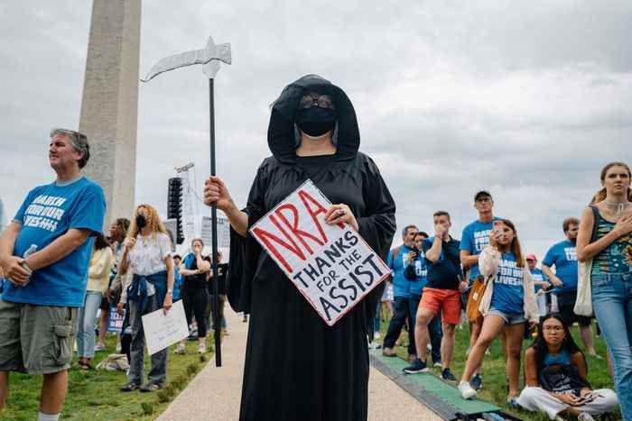 Une femme portant un costume de Grim Reaper et tenant une pancarte qui dit 