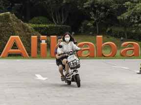 Un couple conduit un scooter devant la signalisation au siège social d'Alibaba Group Holding Ltd. à Hangzhou, en Chine.