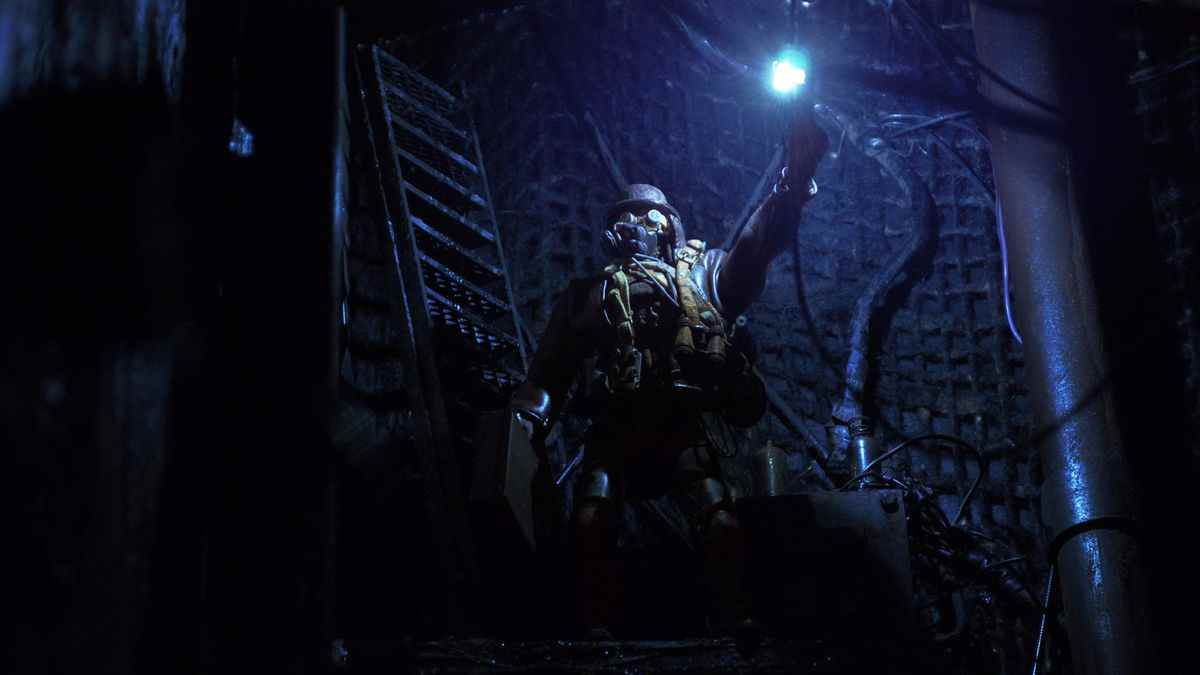 Un assassin portant un masque à gaz tient une lumière dans un couloir souterrain sombre de Mad God.