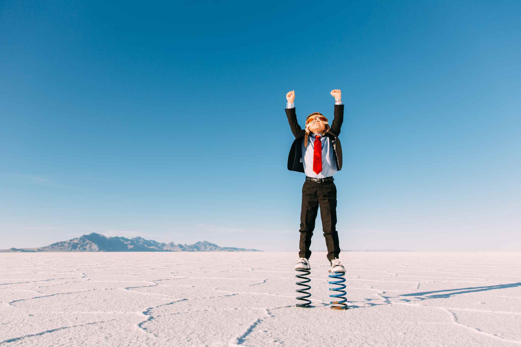 Un jeune garçon d'affaires vêtu d'un costume, d'une casquette de vol et de lunettes se dresse sur des ressorts dans le désert de l'Utah.  faire grandir l'entreprise pour les startups saas