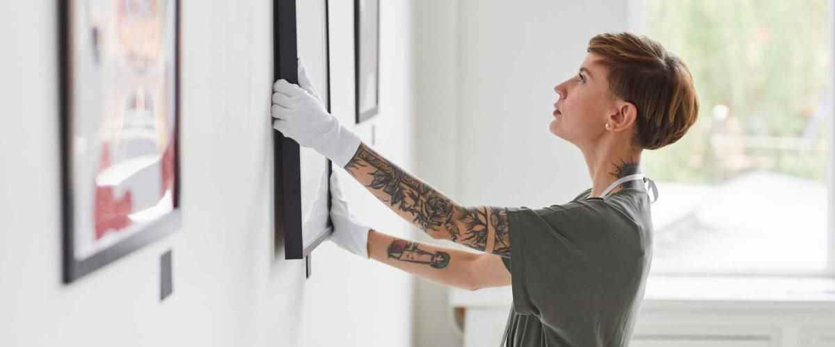 Portrait de vue latérale d'une femme créative tatouée accrochant des peintures au mur lors de la planification d'une exposition de galerie d'art, espace de copie