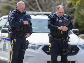 Deux agents de la GRC observent une minute de silence en l'honneur du const.  Heidi Stevenson et les 21 autres victimes des massacres à un poste de contrôle sur Portapique Road à Portapique, en Nouvelle-Écosse, le vendredi 24 avril 2020.